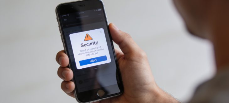Personne tenant telephone avec ecran d'alerte securite affichee.